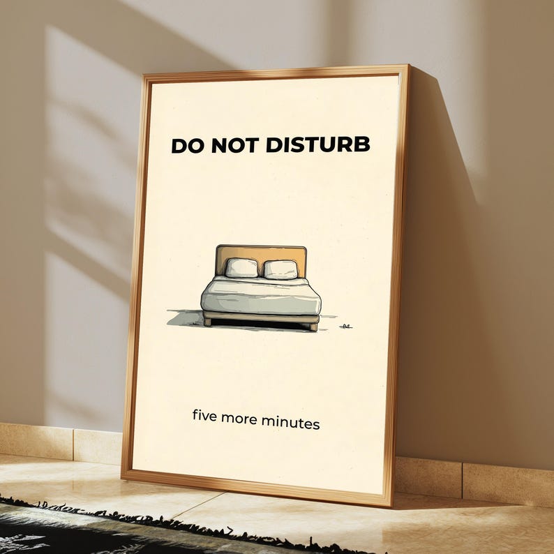 Puede incluir: Un cuadro enmarcado con una ilustraci&oacute;n de dibujos animados de una cama. Las palabras "DO NOT DISTURB" est&aacute;n en la parte superior, y "five more minutes" en la inferior. El marco es de color marr&oacute;n claro.