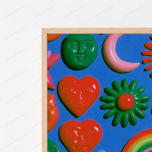 May include: A framed wall art piece featuring a vibrant blue background with raised, glossy, three-dimensional shapes including a green moon face, a pink crescent moon, a red heart face, a green flower, and a colorful rainbow segment.