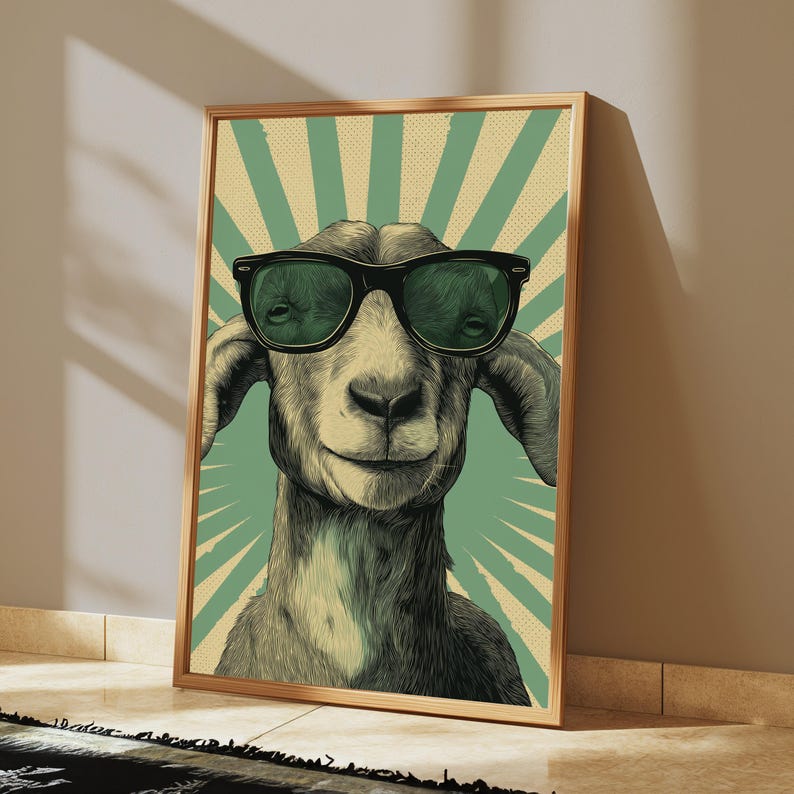 May include: A framed wall art print featuring a detailed illustration of a goat wearing black sunglasses. The goat is centred against a background of alternating light green and cream-coloured sunburst rays with a subtle dotted texture pattern.