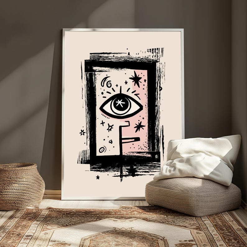 Peut inclure: Une impression d'art mural encadr&eacute;e pr&eacute;sentant un symbole d'&oelig;il graphique noir central entour&eacute; d'&eacute;l&eacute;ments c&eacute;lestes comme des &eacute;toiles et un croissant de lune, sur un fond rose p&acirc;le dans une bordure rectangulaire noire textur&eacute;e.