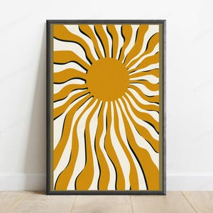 May include: A framed wall art print featuring a central solid mustard yellow circle with radiating wavy lines in alternating mustard yellow, cream, and thin black stripes, creating a sunburst pattern within a dark rectangular frame.