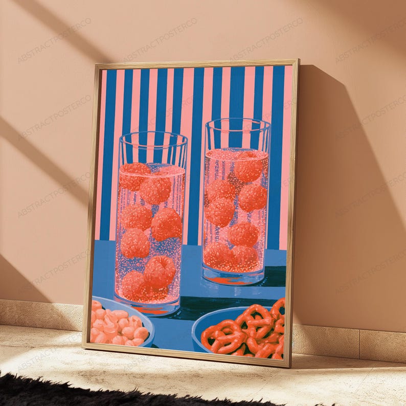 May include: A framed wall art print featuring two tall glasses filled with sparkling liquid and floating red raspberries, set against a background of vertical pink and blue stripes. Below the glasses are two bowls containing snacks.