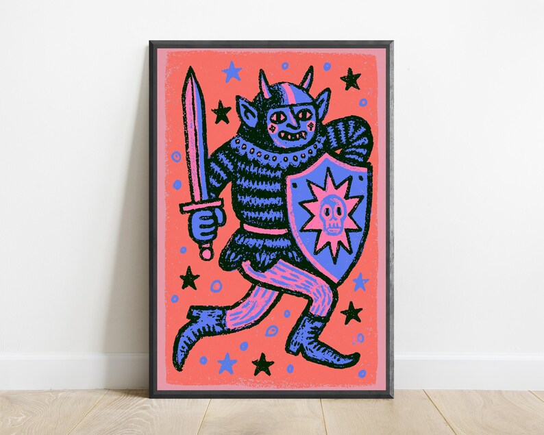 May include: A framed art print featuring a dark blue horned creature in armor, holding a sword and a shield with a pink skull emblem. The background is a vibrant coral color decorated with scattered black and blue stars and small circles.