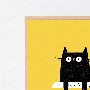 May include: A framed wall art print featuring a black cat illustration with a textured appearance against a solid yellow background. The cat has large white circular eyes, a small pink nose, and long black whiskers. The frame is light wood.