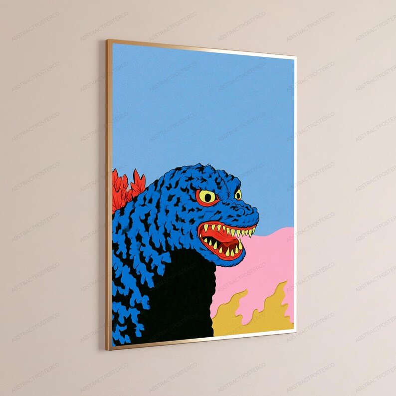 May include: A framed vertical wall art print featuring a stylised blue monster with a black chest, yellow eyes, and sharp teeth. The creature has red dorsal fins against a light blue sky and a pink and yellow landscape background.