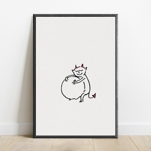 May include: A framed wall art print featuring a minimalist black line drawing of a small devil character with red horns and a red-tipped tail, shown hugging a large circular shape against a plain white background within a thin black frame.