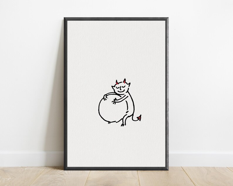 May include: A framed wall art print featuring a minimalist black line drawing of a small devil character with red horns and a red-tipped tail, shown hugging a large circular shape against a plain white background within a thin black frame.
