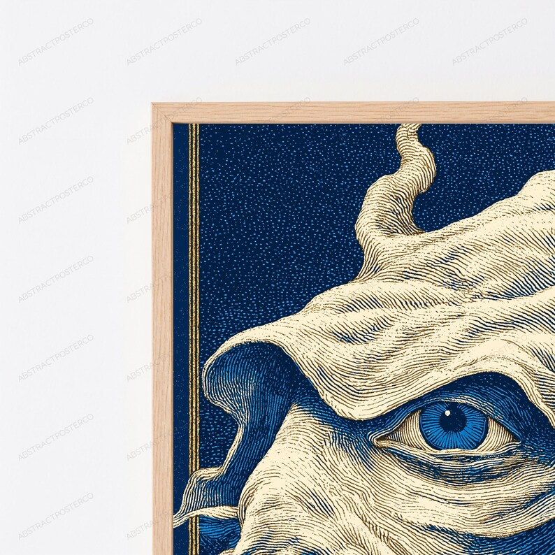 May include: A framed wall art print featuring a detailed illustration of a single blue eye surrounded by cream-colored, flowing fabric-like textures. The background is a deep navy blue with a stippled effect, framed by a light wood border.