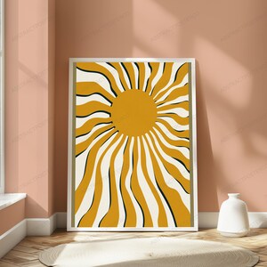 May include: A rectangular framed wall art print featuring a central solid mustard yellow circle surrounded by radiating wavy lines in alternating mustard yellow, cream, and thin black colors, enclosed within a simple white frame border.