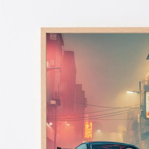 May include: A framed wall art print depicting a rainy city street scene at dusk. The image features a dark car in the foreground, silhouetted buildings, glowing orange neon signage, and overhead power lines against a hazy, muted atmosphere.