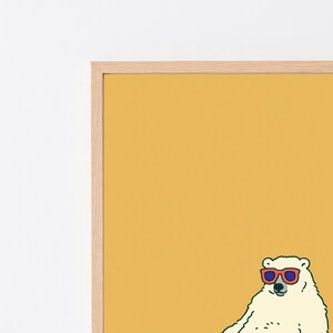 May include: A framed wall art print featuring a white polar bear illustration against a solid mustard yellow background. The bear is wearing red-rimmed sunglasses with dark lenses. The artwork is encased in a light-toned wooden frame.