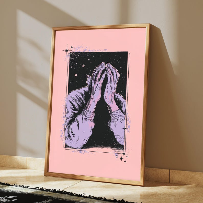 May include: A framed art print featuring a black and white line drawing of a figure with hands covering their face, set against a starry night sky background. The illustration is enclosed in a rectangular border on a solid light pink background.