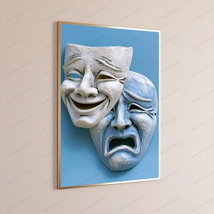 May include: A framed wall art print featuring two theatrical masks against a solid light blue background. The top mask is white with a joyful expression, while the overlapping bottom mask is light blue with a sorrowful, downturned expression.