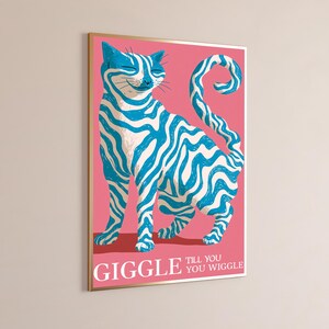 May include: A rectangular wall art print featuring a cat with blue and white wavy stripes against a solid pink background. The cat has a curled tail and a smiling expression. The text GIGGLE TILL YOU WIGGLE is printed in white at the bottom.
