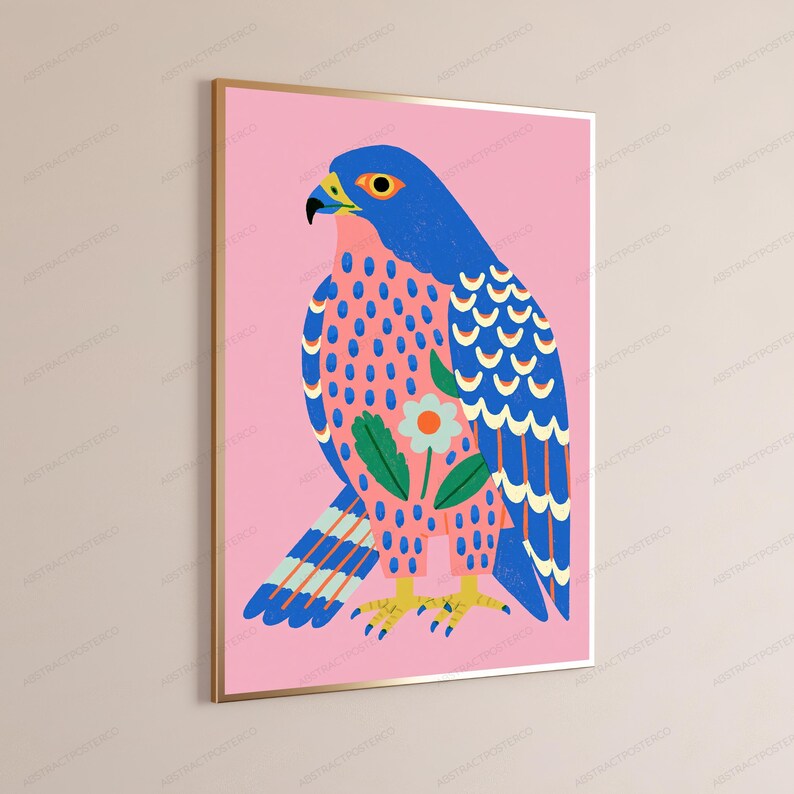 May include: A framed wall art print featuring a stylized blue falcon against a solid pink background. The bird has a yellow beak, orange eye, and a patterned chest with a central white flower and green leaves. The wings display blue and white feathers.