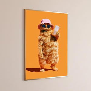 May include: A framed wall art print featuring an orange tabby cat standing upright against a solid orange background. The cat wears a light pink bucket hat and dark round sunglasses while holding a clear glass filled with ice cubes in one paw.
