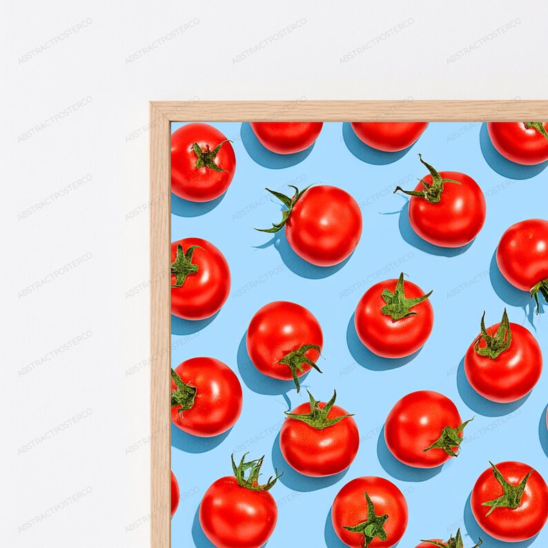 May include: A framed wall art print featuring a repeating pattern of bright red tomatoes with green stems arranged on a solid light blue background. The frame is made of light-colored wood with a simple, clean profile surrounding the artwork.