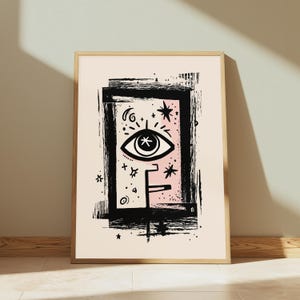 Peut inclure: Une affiche d'art encadr&eacute;e pr&eacute;sentant une illustration &agrave; l'encre noire d'un &oelig;il stylis&eacute; centr&eacute; dans un cadre rectangulaire. Le motif inclut des &eacute;l&eacute;ments c&eacute;lestes comme des &eacute;toiles et des croissants sur un fond rose p&acirc;le, le tout sur papier cr&egrave;me.