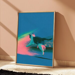 May include: A framed vertical art print featuring a black and white cat leaping through a vibrant blue space. A glowing pink and yellow light trail follows the cat, which is positioned above a distant, blurred city skyline under a dark blue sky.
