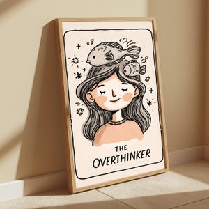 K&ouml;nnte beinhalten: Ein gerahmter Kunstdruck mit einer Cartoon-Illustration einer Person mit langem, welligem Haar und zwei Fischen auf dem Kopf. Der Hintergrund ist cremefarben mit kleinen Sternakzenten. Der Text unten lautet THE OVERTHINKER.