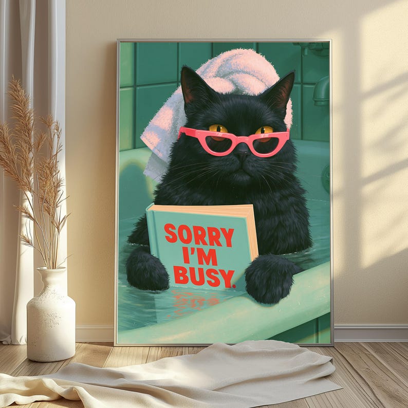 May include: A framed wall art print featuring a black cat with yellow eyes wearing bright pink cat-eye glasses and a white towel on its head. The cat is sitting in a green bathtub holding a light blue book with the red text SORRY I'M BUSY.