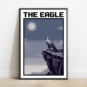 May include: A framed pixel art print titled THE EAGLE, featuring a white and grey eagle perched on a dark rocky cliff overlooking a misty landscape under a pale moon. The artwork uses a limited colour palette of blues, greys, and whites.