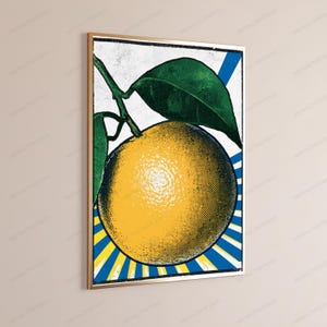 May include: A framed wall art print featuring a pop art style illustration of a yellow orange with green leaves. The background consists of blue and yellow radiating sunburst lines. The image has a textured, vintage halftone dot pattern.