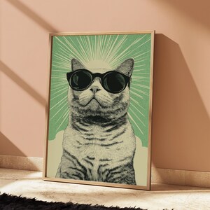 Puede incluir: Una l&aacute;mina de arte mural rectangular con una ilustraci&oacute;n detallada de un gato con gafas de sol negras. El gato est&aacute; centrado sobre un fondo verde claro con l&iacute;neas de rayos de sol y una base de color crema, todo dentro de un marco de madera.