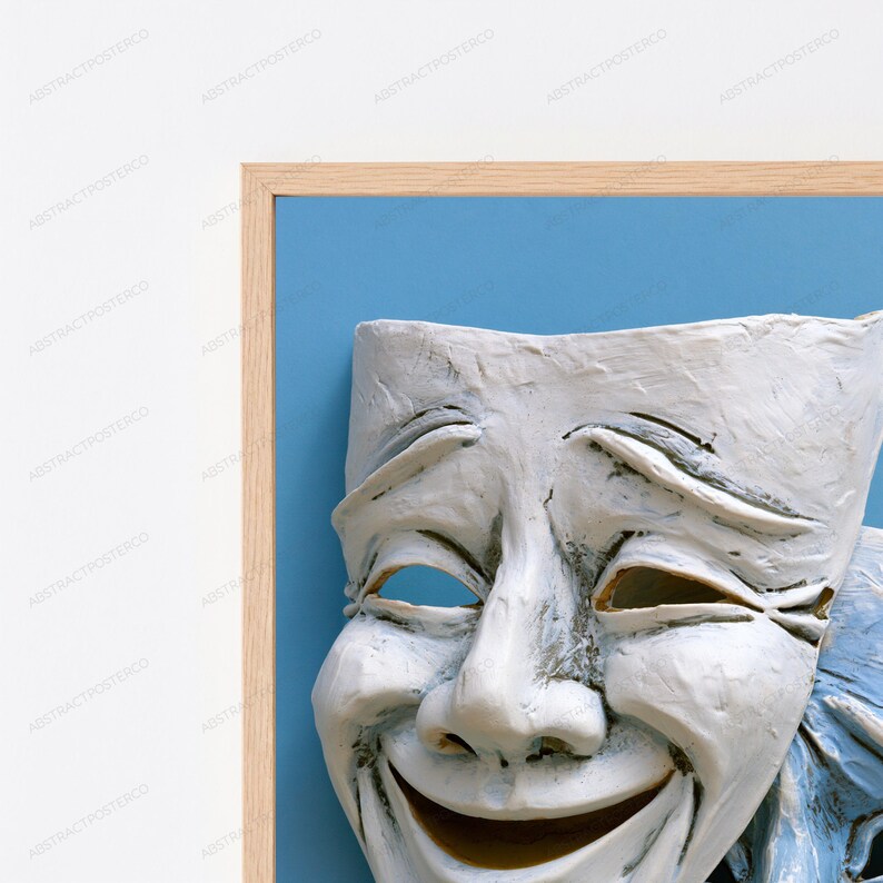 May include: A framed wall art piece featuring a white, textured theatrical comedy mask with a wide, smiling expression. The mask is set against a solid light blue background and enclosed within a light-toned wooden frame with a clean, simple edge.