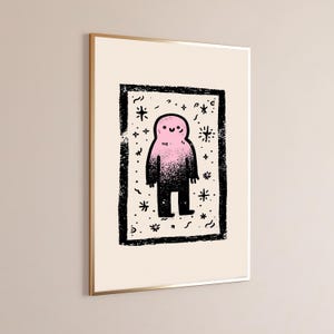 May include: A framed wall art print featuring a central pink and black gradient figure with a simple smiling face. The figure is surrounded by black hand-drawn stars and squiggles on a cream background, all enclosed within a thick black border.