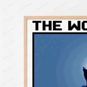 May include: A framed wall art print featuring a pixelated graphic of a wolf howling at a large, bright moon against a dark blue background. The text THE WO is visible at the top in a bold, black, pixelated font, encased in a light wood frame.