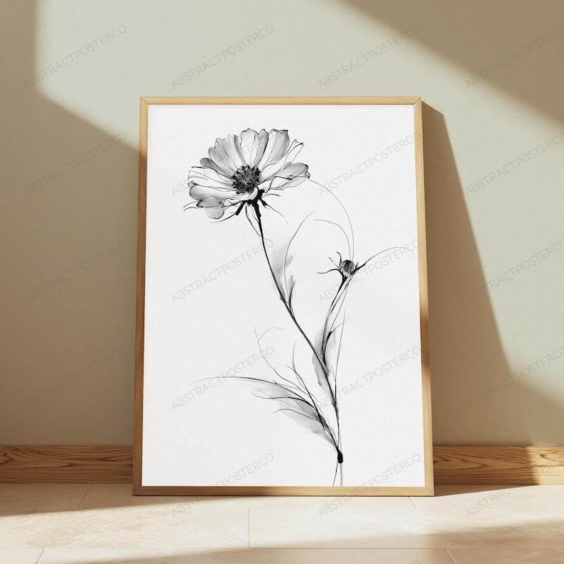 May include: A framed wall art print featuring a black and white botanical illustration of a single cosmos flower in full bloom with a smaller bud on a thin stem. The artwork is presented in a light-coloured wooden frame against a neutral wall.