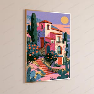 May include: A framed vertical art print depicting a pink Mediterranean-style villa with arched windows, a balcony, and a staircase. The scene includes orange trees, tall green cacti, and a yellow sun set against a purple and pink sky.