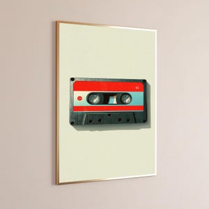 May include: A framed wall art print featuring a centered illustration of a cassette tape. The tape has a black plastic body, a bright red label section, and a light blue center strip. The number 62 is printed in white on the red label area.
