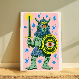 May include: A rectangular art print featuring a stylised illustration of a horned warrior figure in blue and green, holding a sword and a shield with an eye motif. The background is light pink with scattered blue stars and a yellow sunburst.