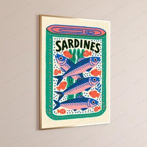 May include: A rectangular wall art print featuring a stylized illustration of an open tin of sardines. The design includes three large blue and pink fish, several smaller orange fish, and green seaweed accents on a cream background with the text SARDINES.
