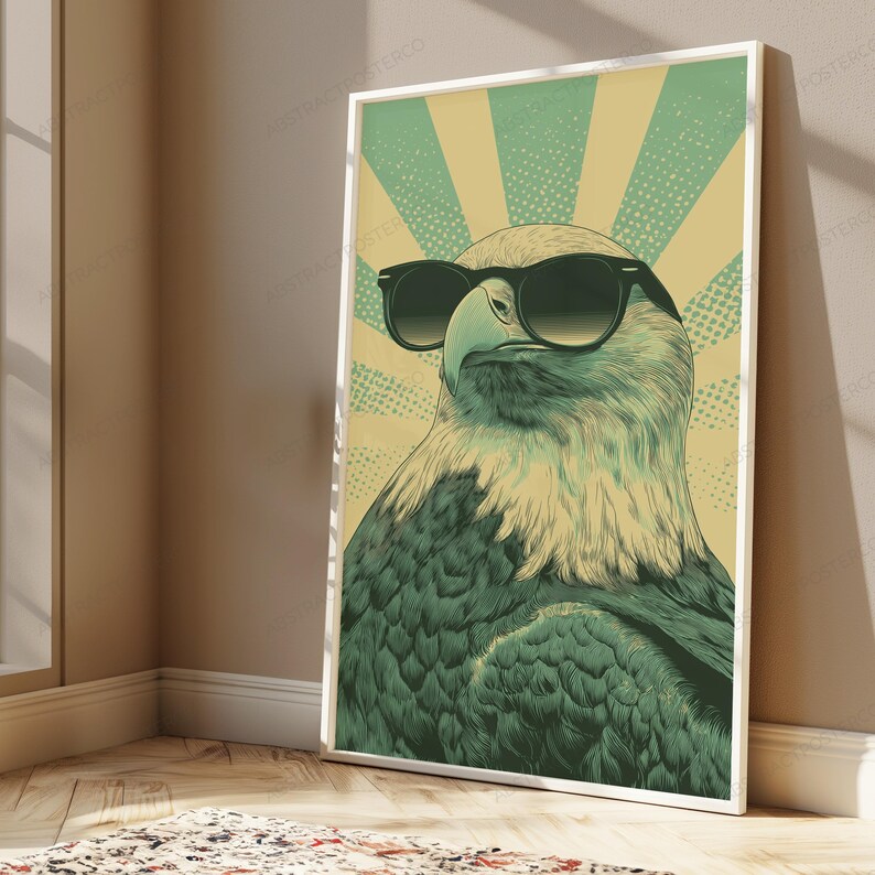 May include: A framed vertical wall art print featuring a stylized illustration of a bald eagle wearing black sunglasses. The eagle is rendered in shades of dark green and cream, set against a background of radiating cream and green sunburst rays.