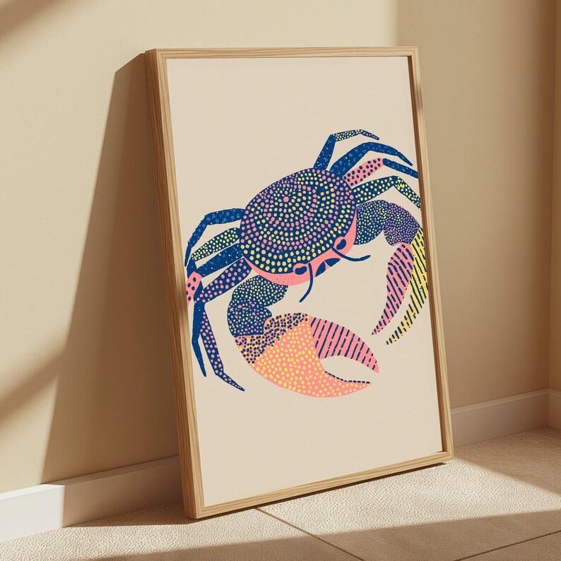 May include: A framed wall art print featuring a stylized crab illustration on a light beige background. The crab is rendered with a mix of blue, pink, and yellow patterns, including dots and stripes, contained within a simple light wood frame.