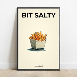 May include: A framed wall art print featuring a cream background with the black text BIT SALTY at the top and standard at the bottom. In the center is a hand-drawn illustration of golden-brown french fries in a white paper container.