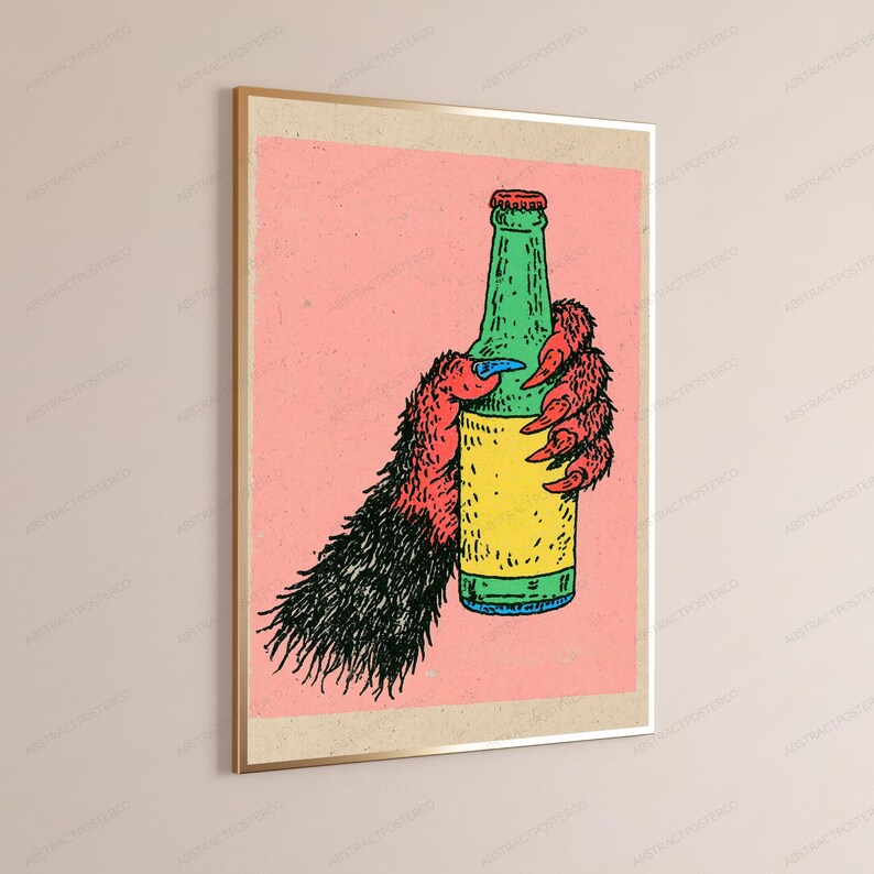 May include: A framed wall art print featuring a stylised illustration of a furry, red and black creature's hand with sharp claws gripping a green glass bottle with a yellow label, set against a solid light pink background within a thin gold frame.