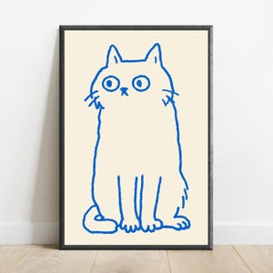 May include: A framed wall art print featuring a simple, hand-drawn illustration of a cat in bright blue ink on a cream-colored background. The cat is depicted in a seated position with wide, circular eyes and a neutral expression, enclosed in a thin black frame.