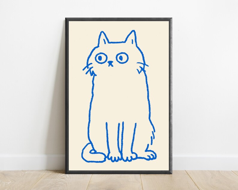 May include: A framed wall art print featuring a simple, hand-drawn illustration of a cat in bright blue ink on a cream-colored background. The cat is depicted in a seated position with wide, circular eyes and a neutral expression, enclosed in a thin black frame.