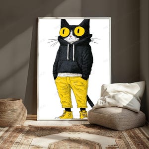 K&ouml;nnte beinhalten: Ein gerahmter Wandkunstdruck, der eine schwarze Katze mit gro&szlig;en gelben Augen zeigt, die einen schwarzen Kapuzenpullover mit wei&szlig;en Kordeln, eine leuchtend gelbe Hose und passende gelbe High-Top-Sneaker tr&auml;gt, vor einem wei&szlig;en Hintergrund.
