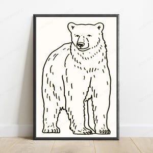 K&ouml;nnte beinhalten: Ein gerahmter Wandkunstdruck mit einer schwarzen Strichzeichnung eines stehenden B&auml;ren auf cremefarbenem Hintergrund. Der B&auml;r ist in einem einfachen Stil mit sichtbaren Felltexturlinien dargestellt und befindet sich in einem d&uuml;nnen schwarzen Rahmen.