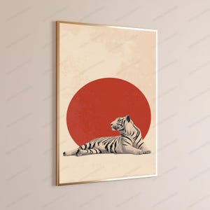 Puede incluir: Una impresi&oacute;n de arte mural rectangular en un marco dorado fino que muestra un tigre blanco con rayas negras tumbado. El tigre est&aacute; colocado frente a un gran c&iacute;rculo rojo s&oacute;lido sobre un fondo beige claro texturizado.