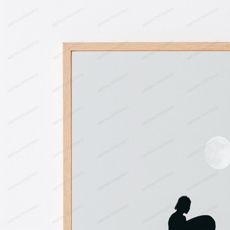 May include: A framed wall art print featuring a light gray background with a white circular moon shape in the upper right corner and a black silhouette of a person holding a surfboard at the bottom, enclosed in a light-colored wooden frame.
