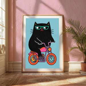 K&ouml;nnte beinhalten: Ein gerahmter Kunstdruck, der eine schwarze Katze mit t&uuml;rkisfarbener Brille auf einem lila Motorrad mit orangefarbenen R&auml;dern und einem pinken Sitz zeigt. Die Katze ist vor einem hellblauen Hintergrund in einem flachen Grafikstil dargestellt.