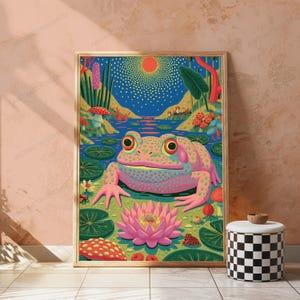 May include: A framed vertical wall art print featuring a vibrant, colorful illustration of a large, spotted pink frog sitting in a pond. The scene includes a bright orange sun, a large pink lotus flower, green lily pads, and red mushrooms.