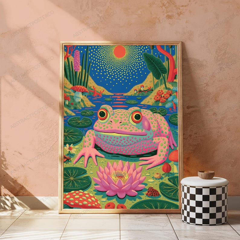 May include: A framed vertical wall art print featuring a vibrant, colorful illustration of a large, spotted pink frog sitting in a pond. The scene includes a bright orange sun, a large pink lotus flower, green lily pads, and red mushrooms.