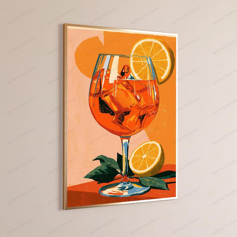 May include: A framed wall art print featuring a vibrant orange cocktail in a stemmed glass filled with ice cubes. A sliced orange garnish sits on the rim, and another orange half rests at the base among green leaves against a warm orange background.